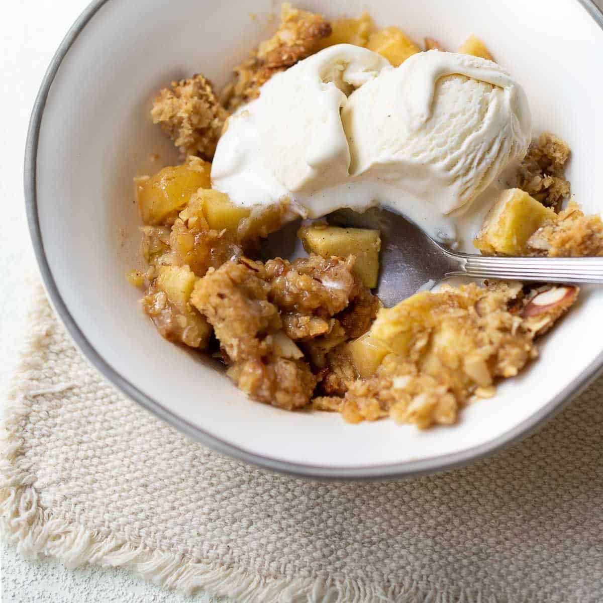 close up image of gluten free apple crisp in bowl topped with ice cream
