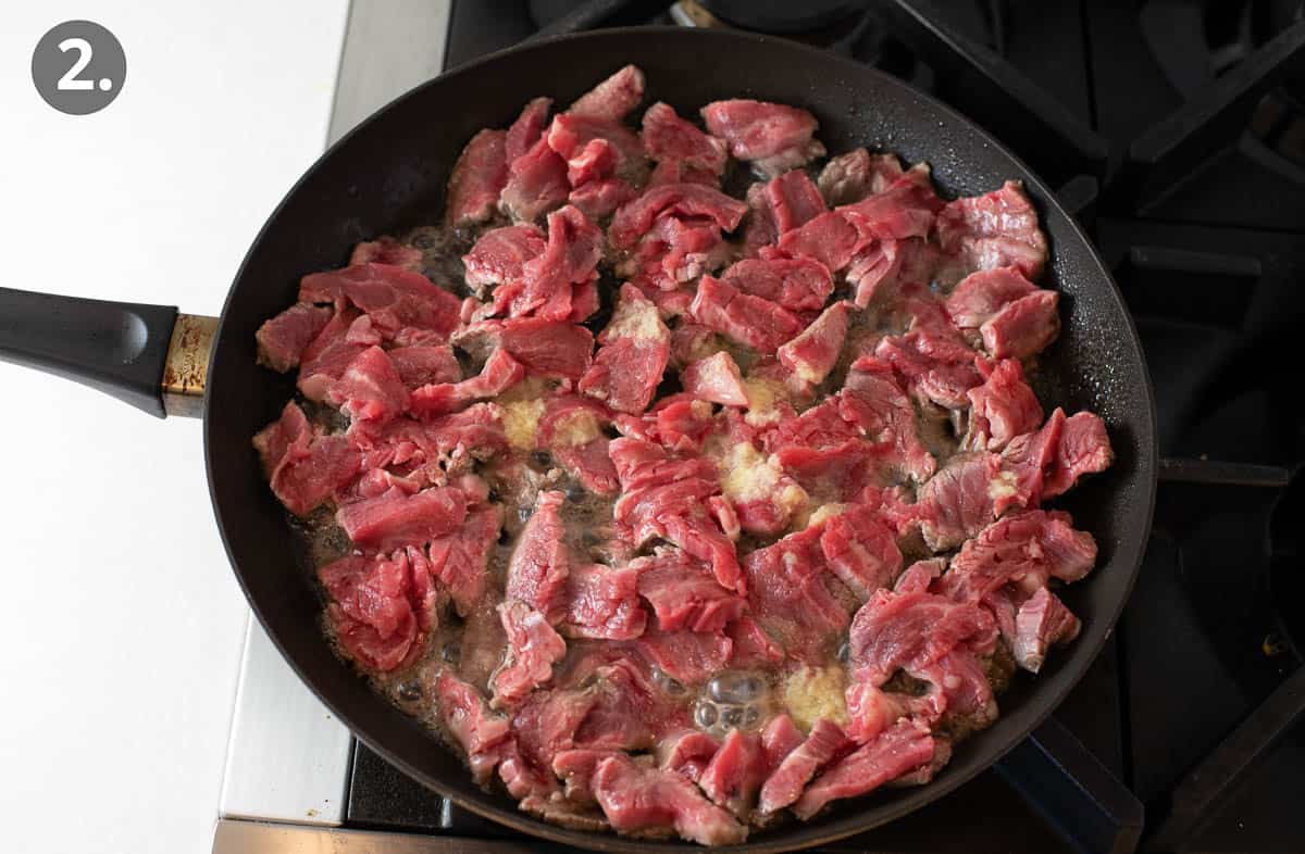 Beef cooking in a skillet, turning from raw to half-way cooked