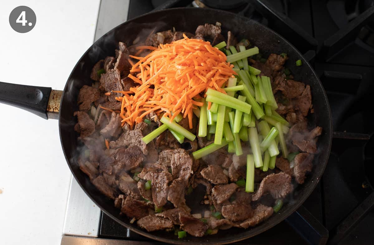 Beef cooking in a skillet, with shredded carrots and peppers on top
