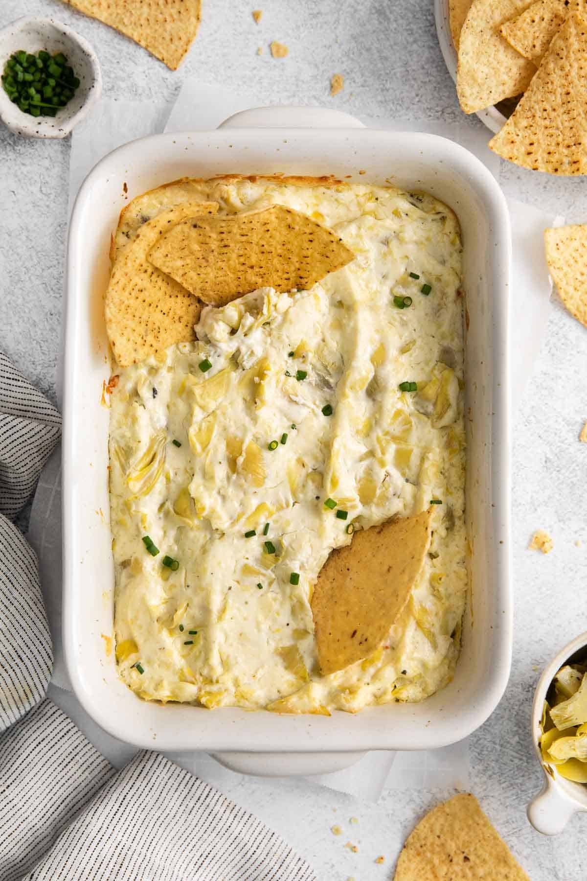 Artichoke dip in a baking dish, with chips in the dip