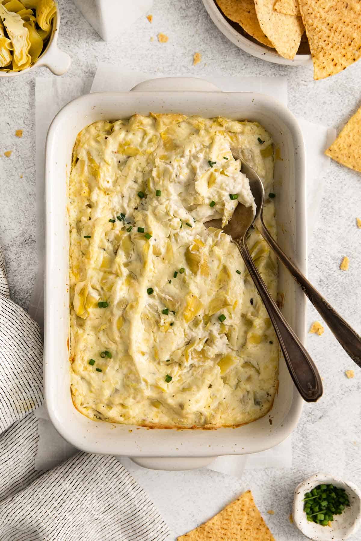 Artichoke dip in a baking dish, with serving spoons placed in the dish