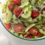 close up of cucumber tomato salad in glass bowl with serving spoon