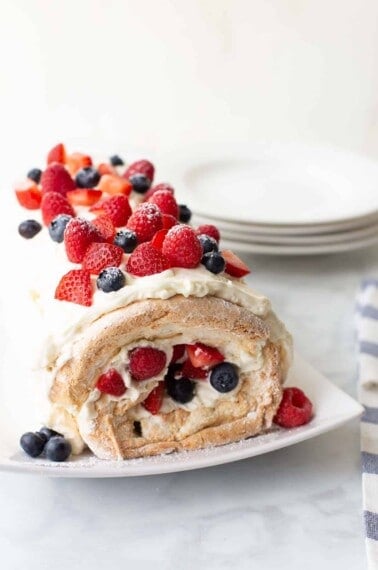 gluten-free angel food acke roll on white serving dish topped with berries