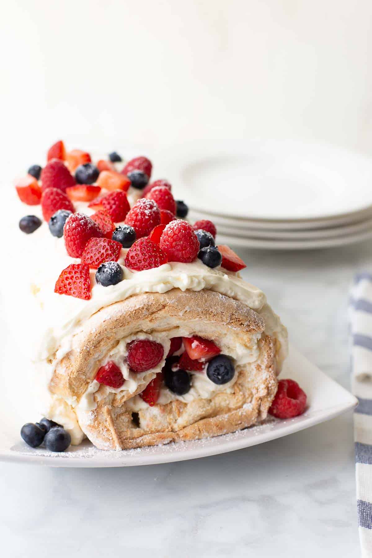 gluten-free angel food cake roll on white serving dish topped with berries