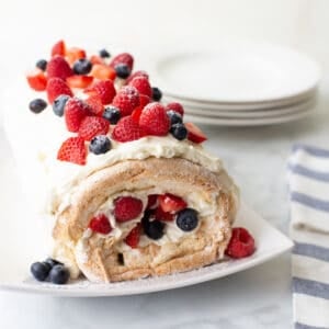 gluten-free angel food cake roll on white serving dish topped with berries