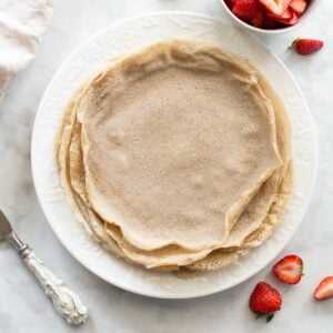 overhead shot of buckwheat crepes on white plate with strawberries