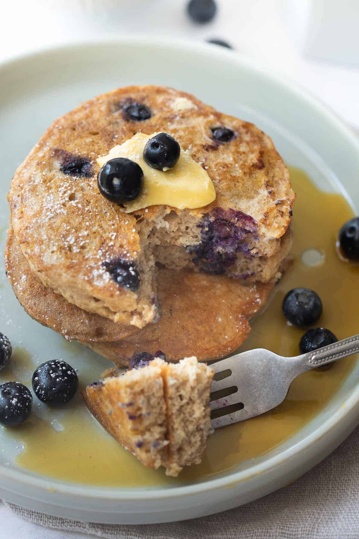close up shot of buckwheat pancakes on white plate with blueberries and maple syrup