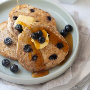 pancakes on gray plate with blueberries, butter and maple syrup and white background
