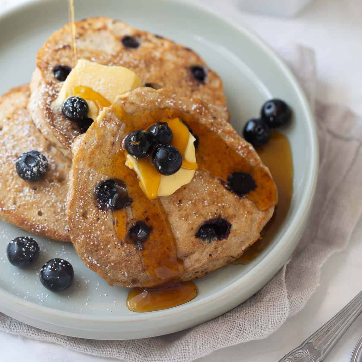 pancakes on gray plate with blueberries, butter and maple syrup and white background