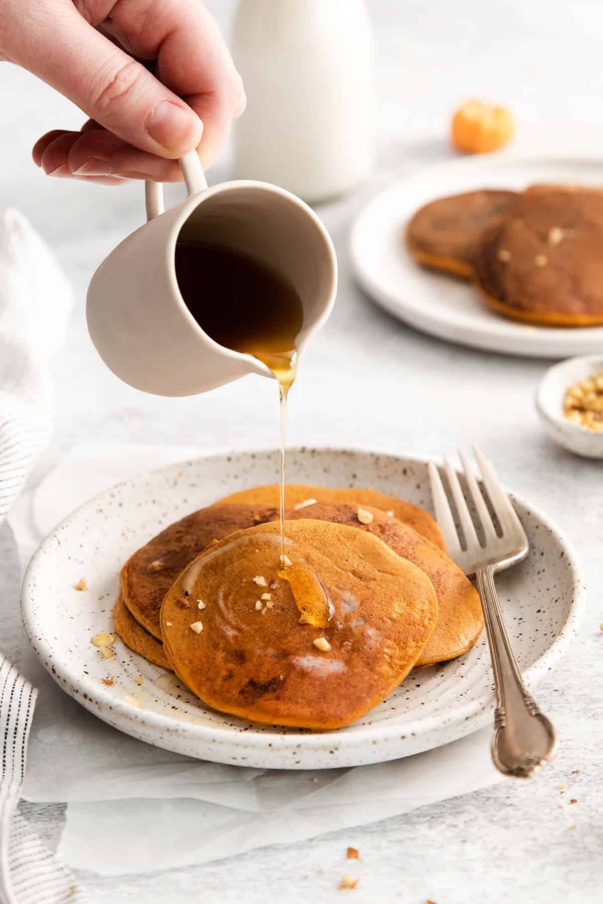 Pumpkin pancakes on a plate, and a hand pouring syrup over the top