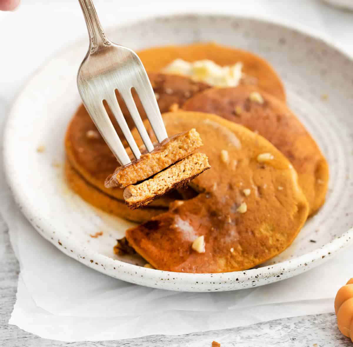 A fork picking up a bite of pumpkin pancakes from a plate