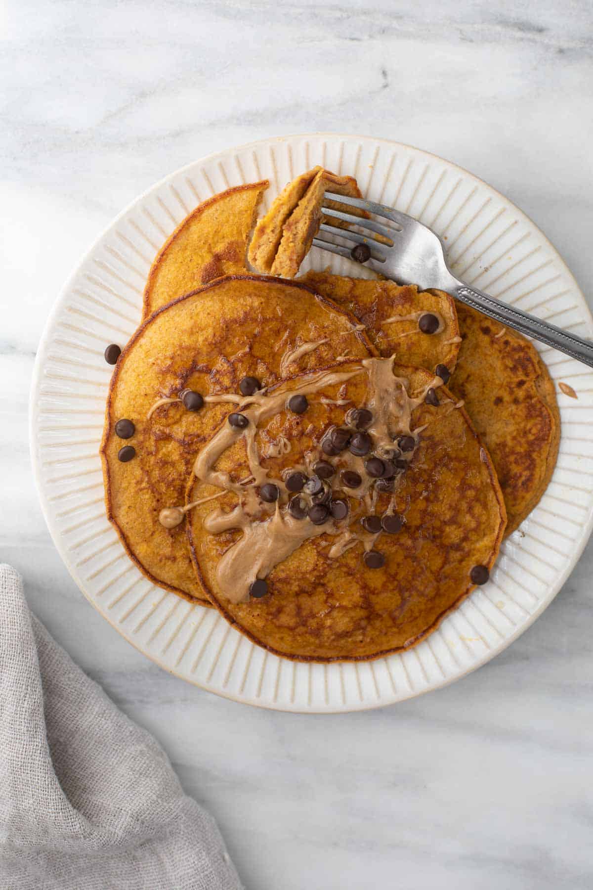 overhead shot of pumpkin spice pancakes on white plate topped with peanut butter and chocolate chips