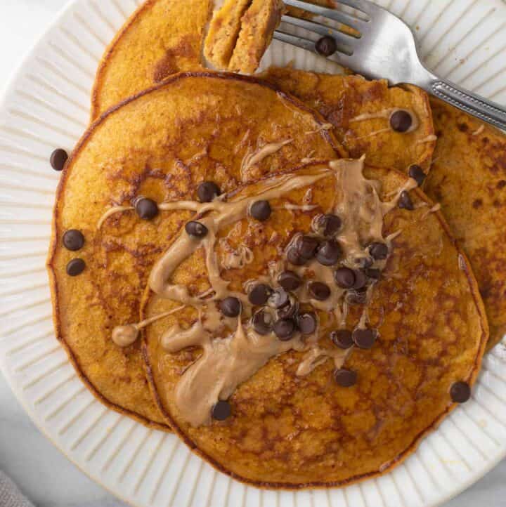 close up overhead shot of pumpkin pancakes on white plate topped with peanut butter and chocolate chips