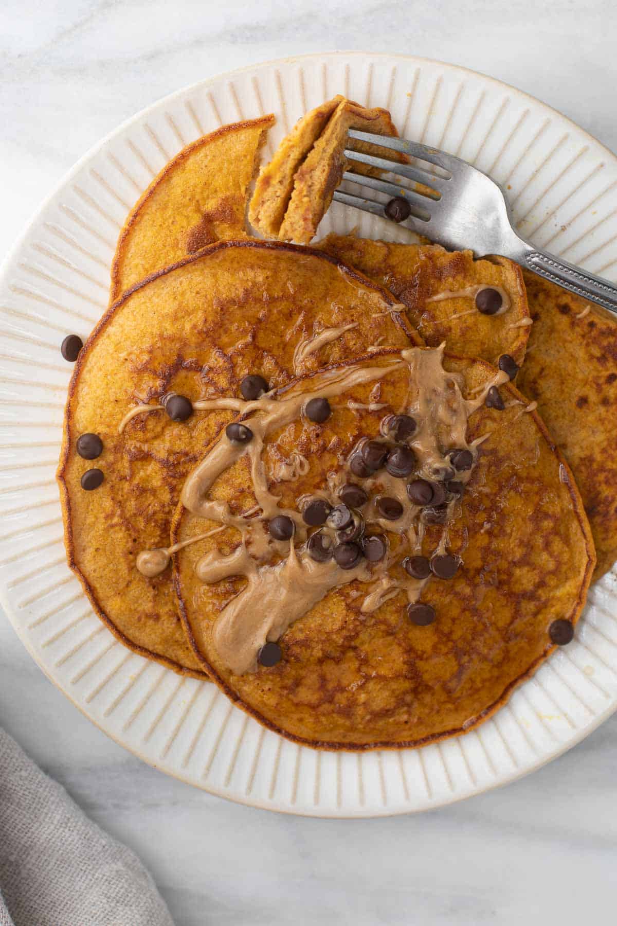 close up overhead shot of pumpkin pancakes on white plate topped with peanut butter and chocolate chips