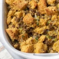 silver spoon scooping sausage stuffing out of white casserole dish