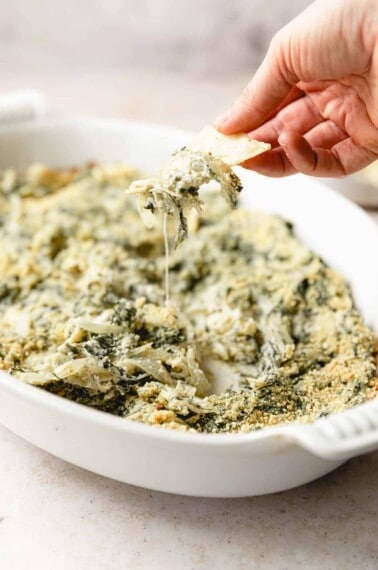 spinach artichoke dip in baking dish with chip for dipping