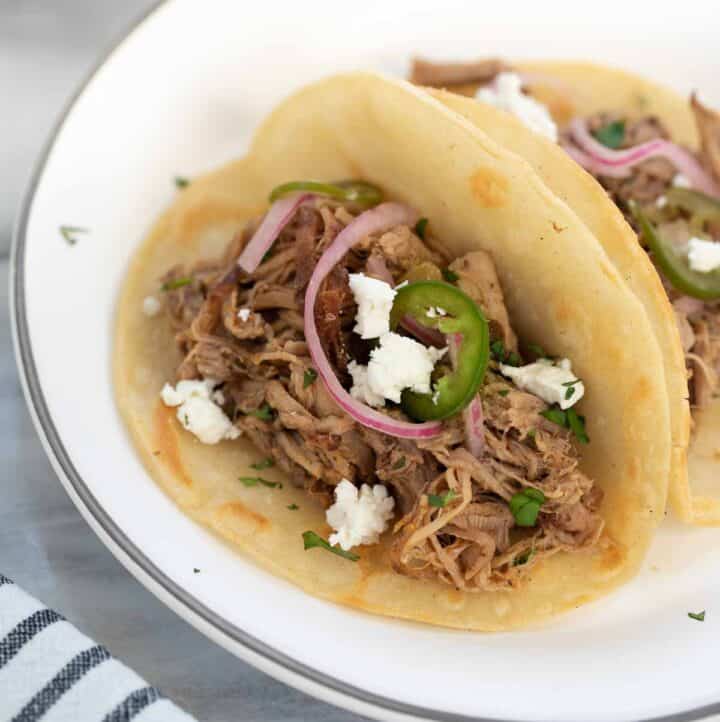 pork taco on white plate topped with pickled onions and cilantro