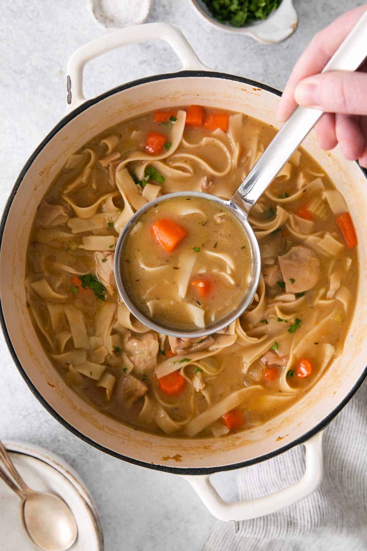 Gluten-free chicken noodle soup in a pot with a ladle scooping out a portion