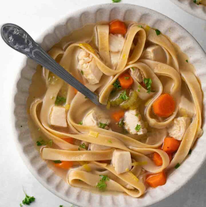 close up shot of gluten free chicken noodle soup in gray bowl topped with parsley and a white napkin