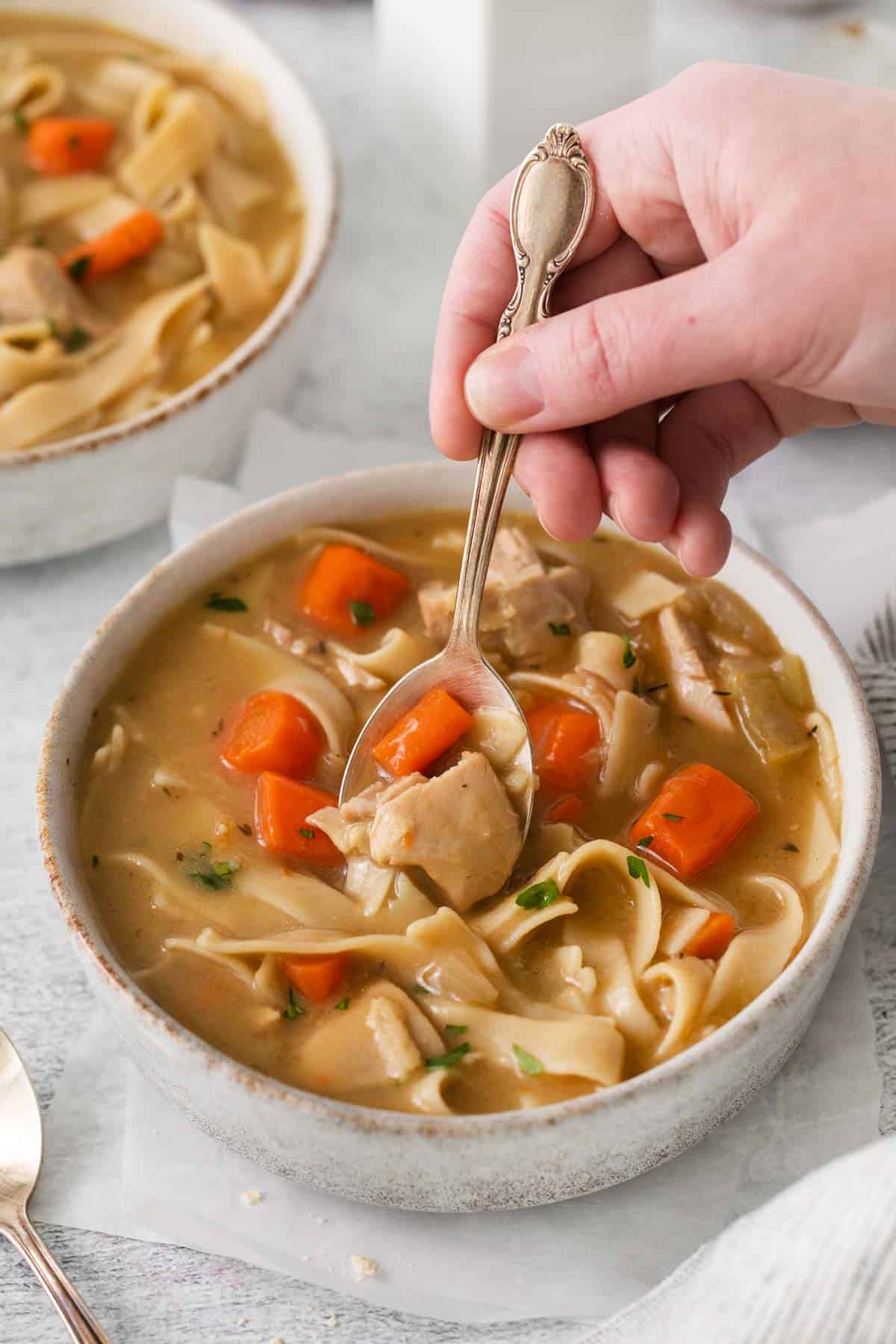 Gluten-free chicken soup in a bowl, and a hand spooning the soup out of the bowl