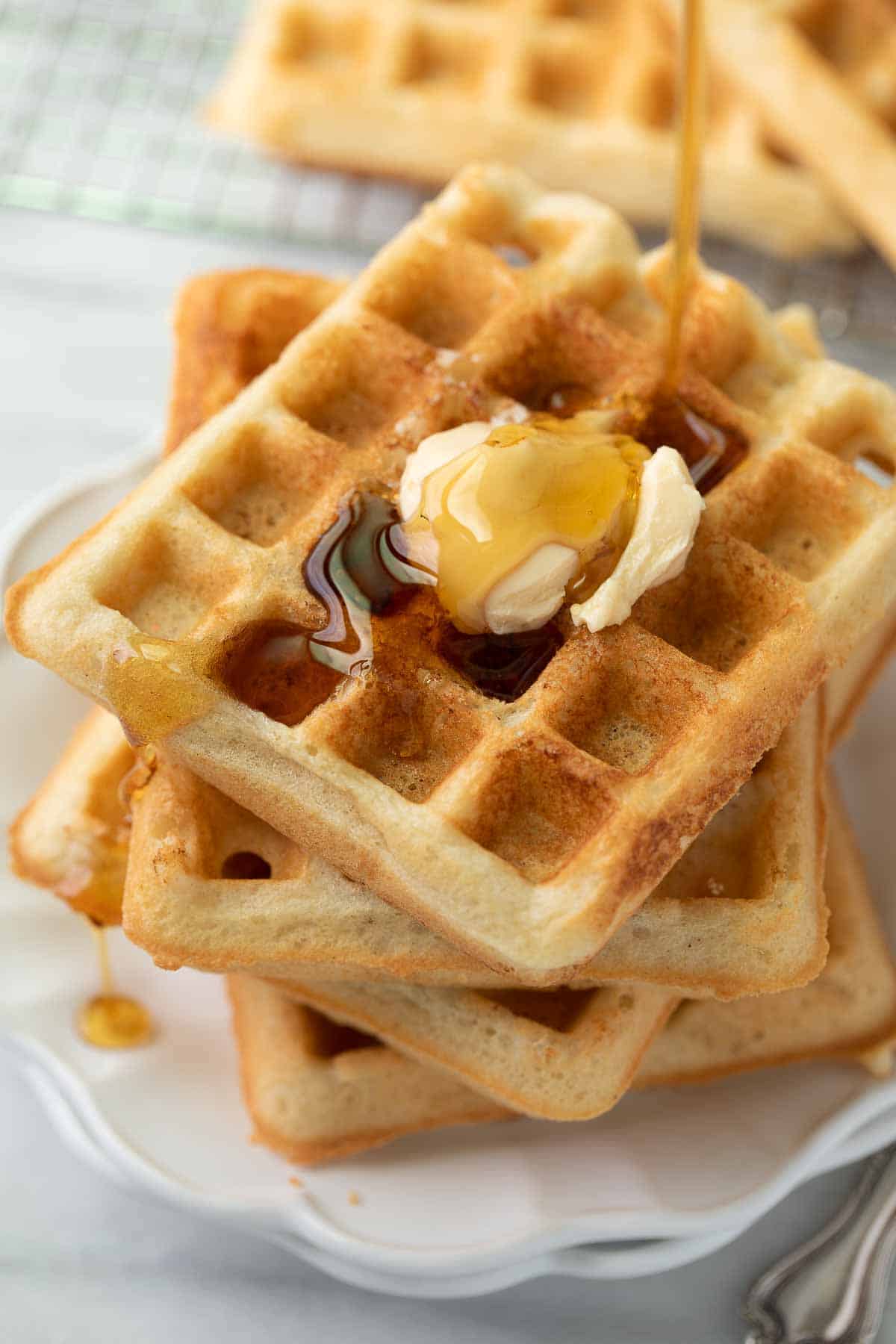 gluten free waffles on white plate with syrup being drizzled over
