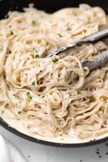 gluten free alfredo sauce over pasta with tongs in black dish