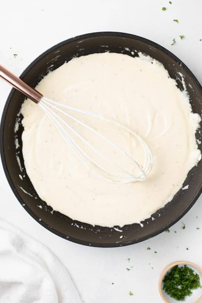 overhead shot of alfredo sauce in black pan with whisk