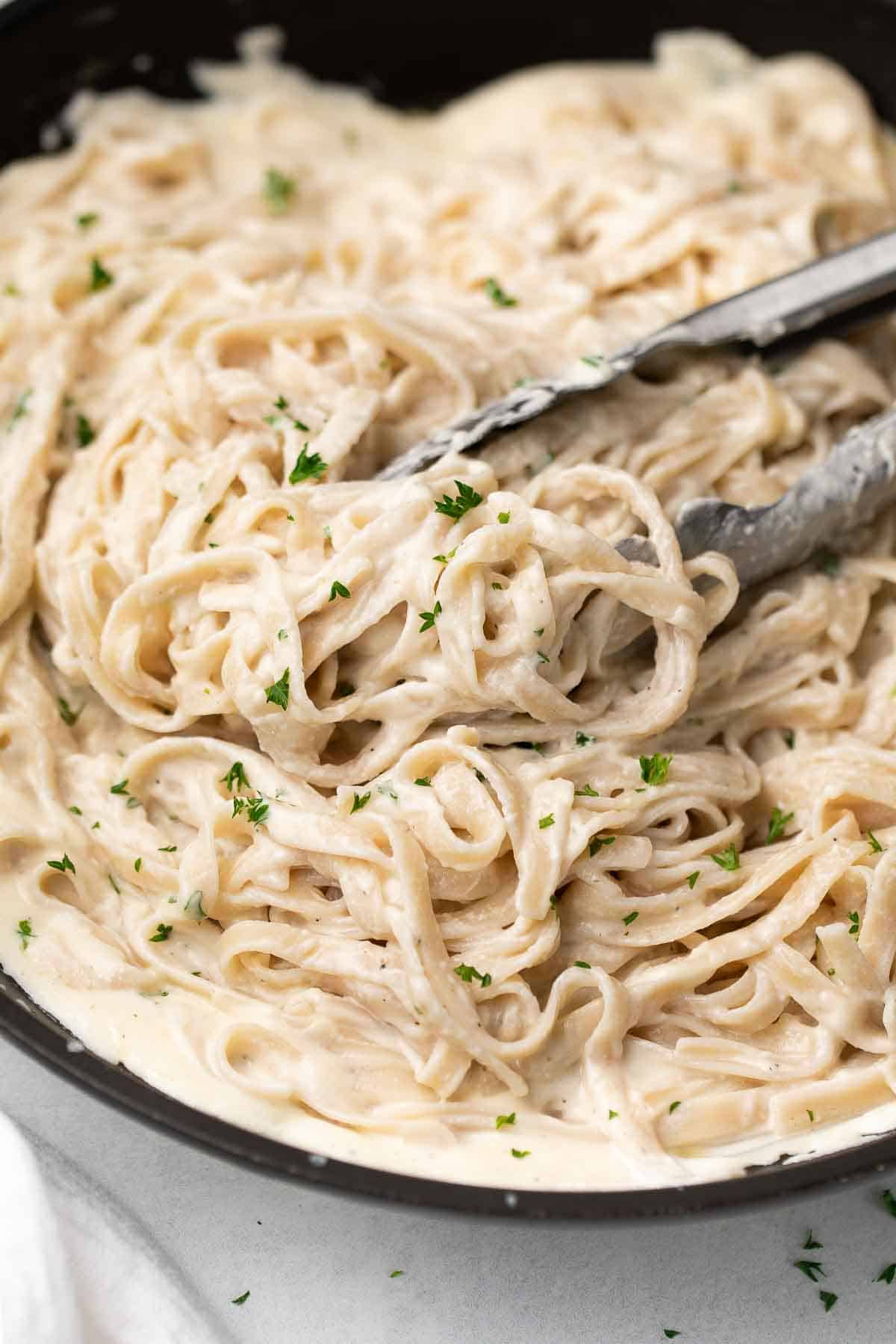 gluten free alfredo sauce over pasta with tongs in black dish