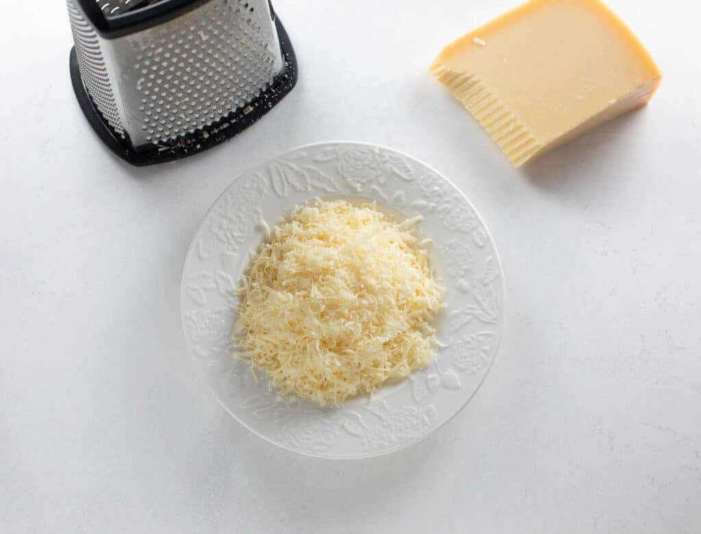 grated parmesan cheese on white plate with cheese grater on white background
