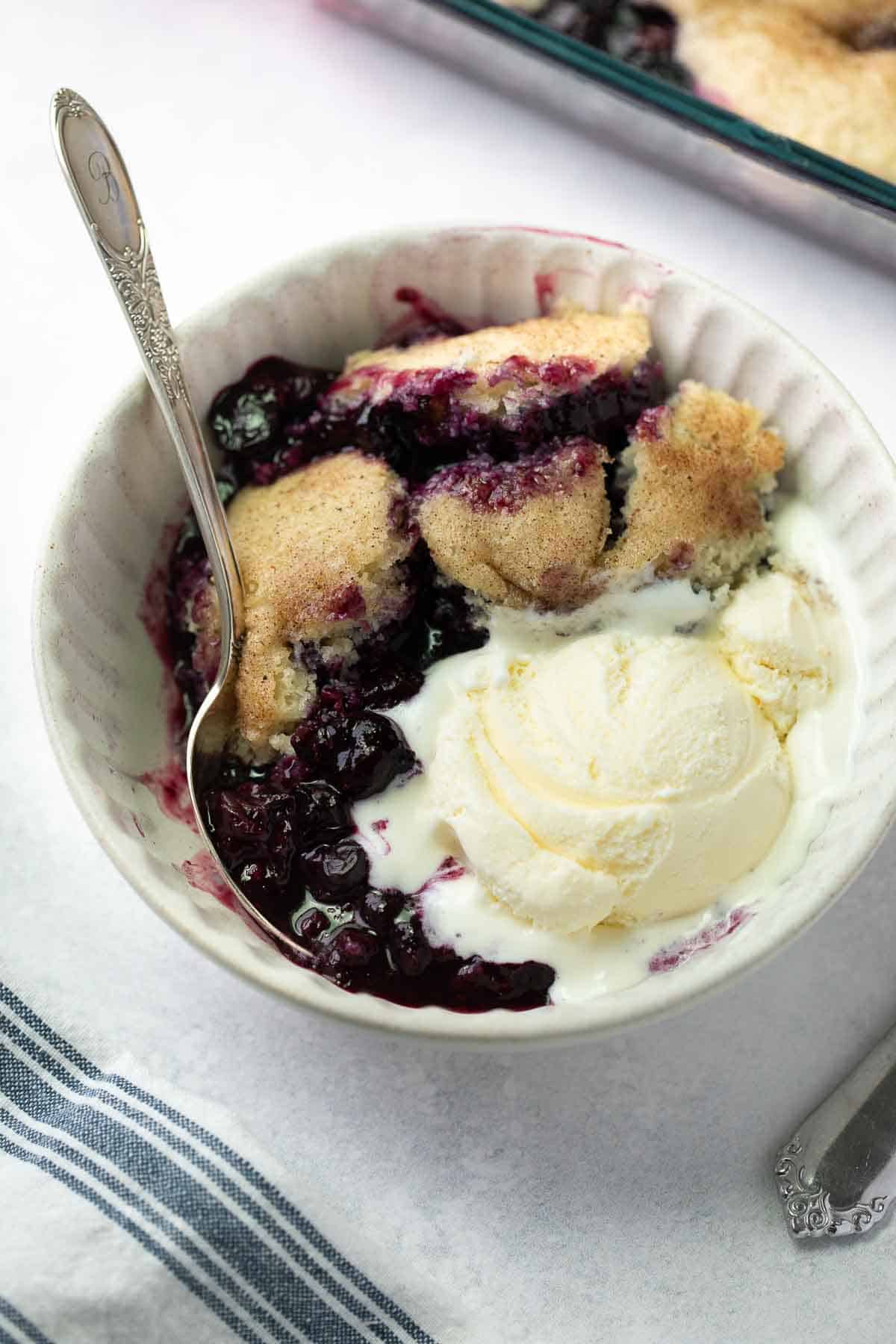 gluten-free blueberry cobbled in white dish topped with ice cream for serving