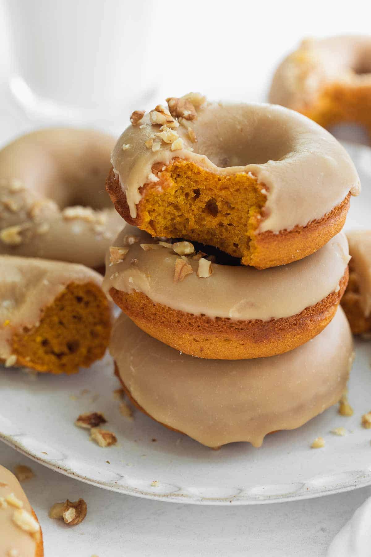gluten free pumpkin donuts stacked on white plate with bite taken out of one