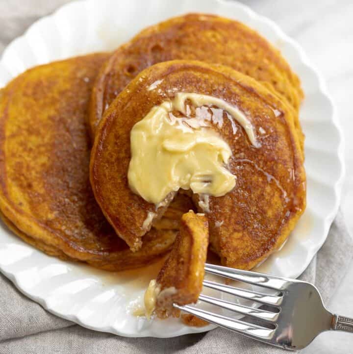 close up image of gluten free pumpkin pancakes on white plate topped with butter and syrup
