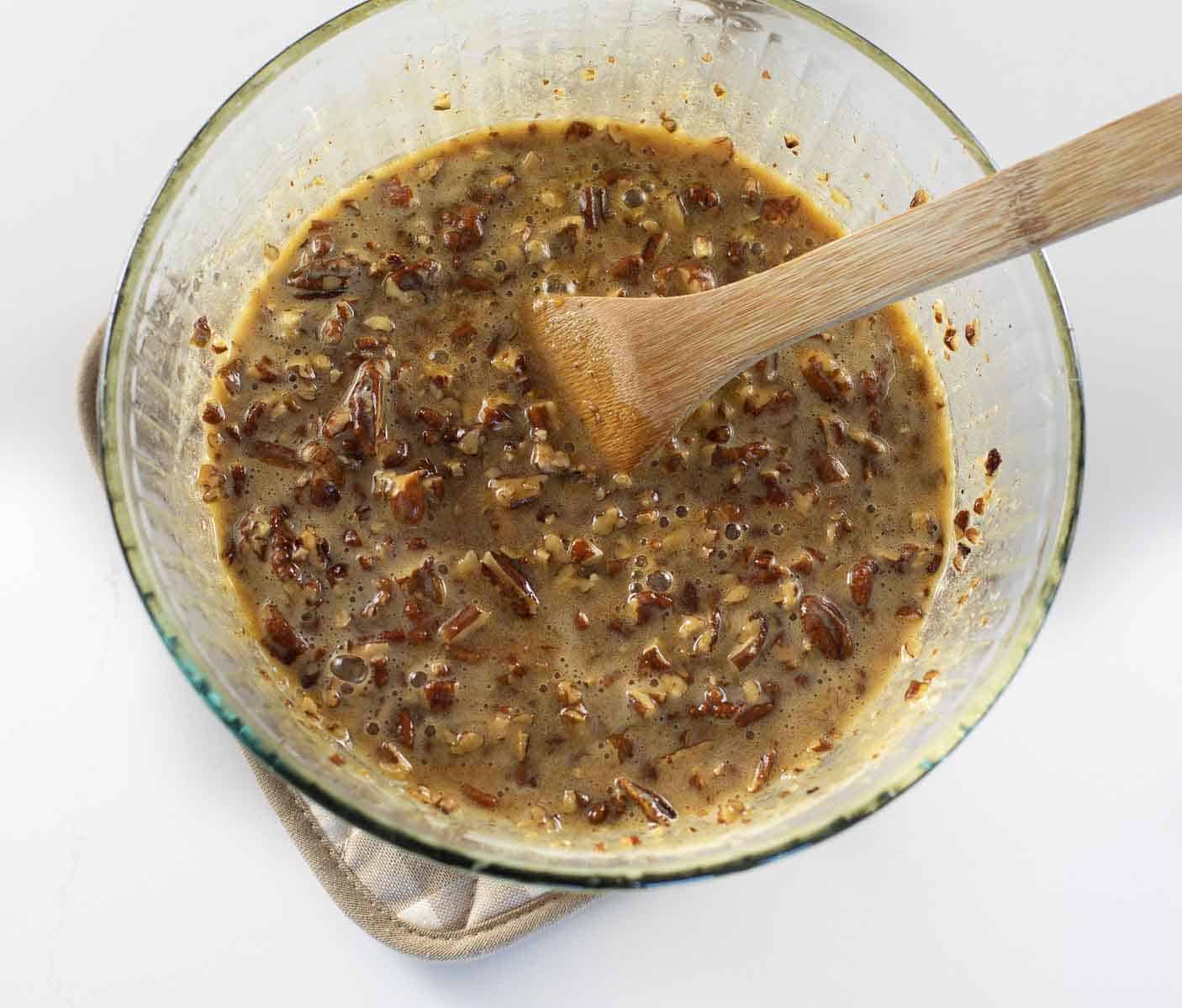 pecan pie filling in glass bowl being stirred with wooden spoon
