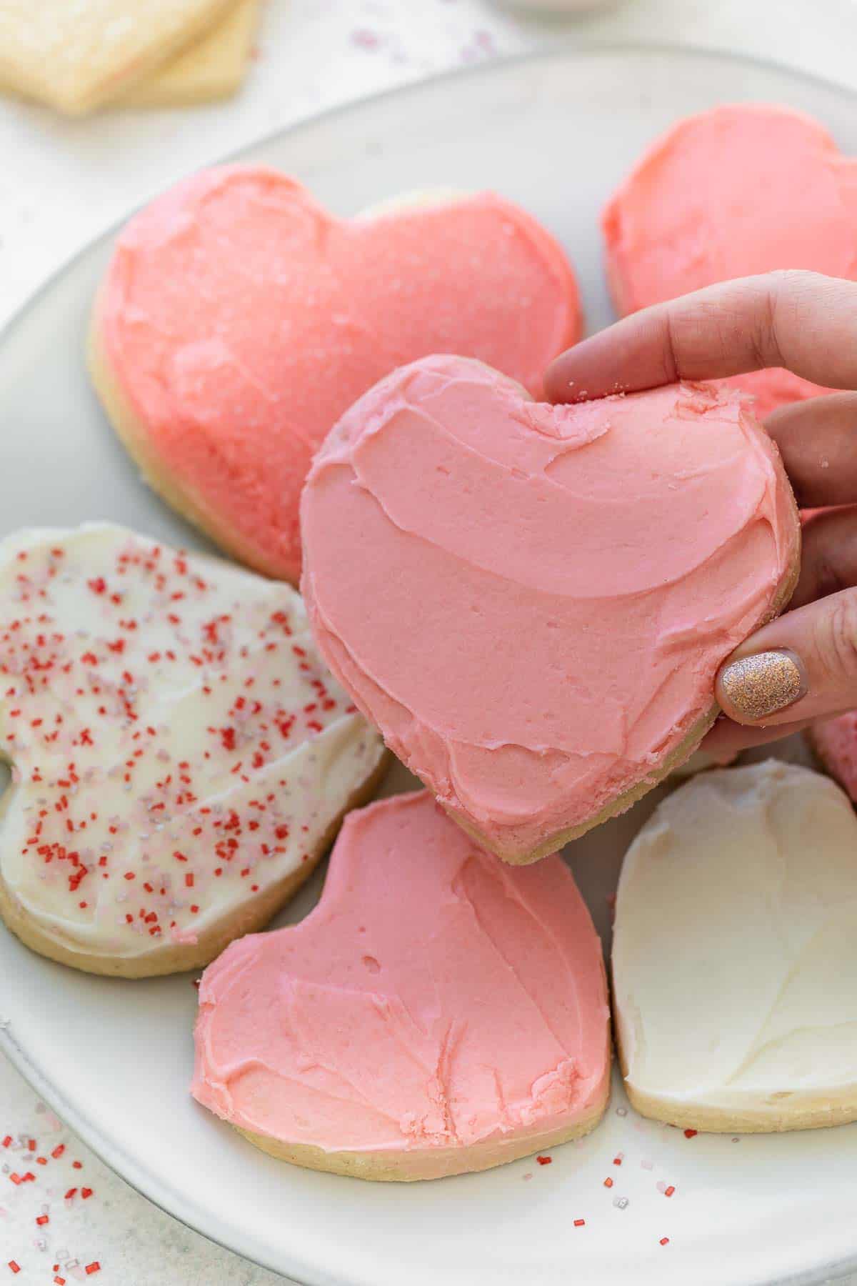 close up of gluten free heart cookie being held with hand over plate of other cookies