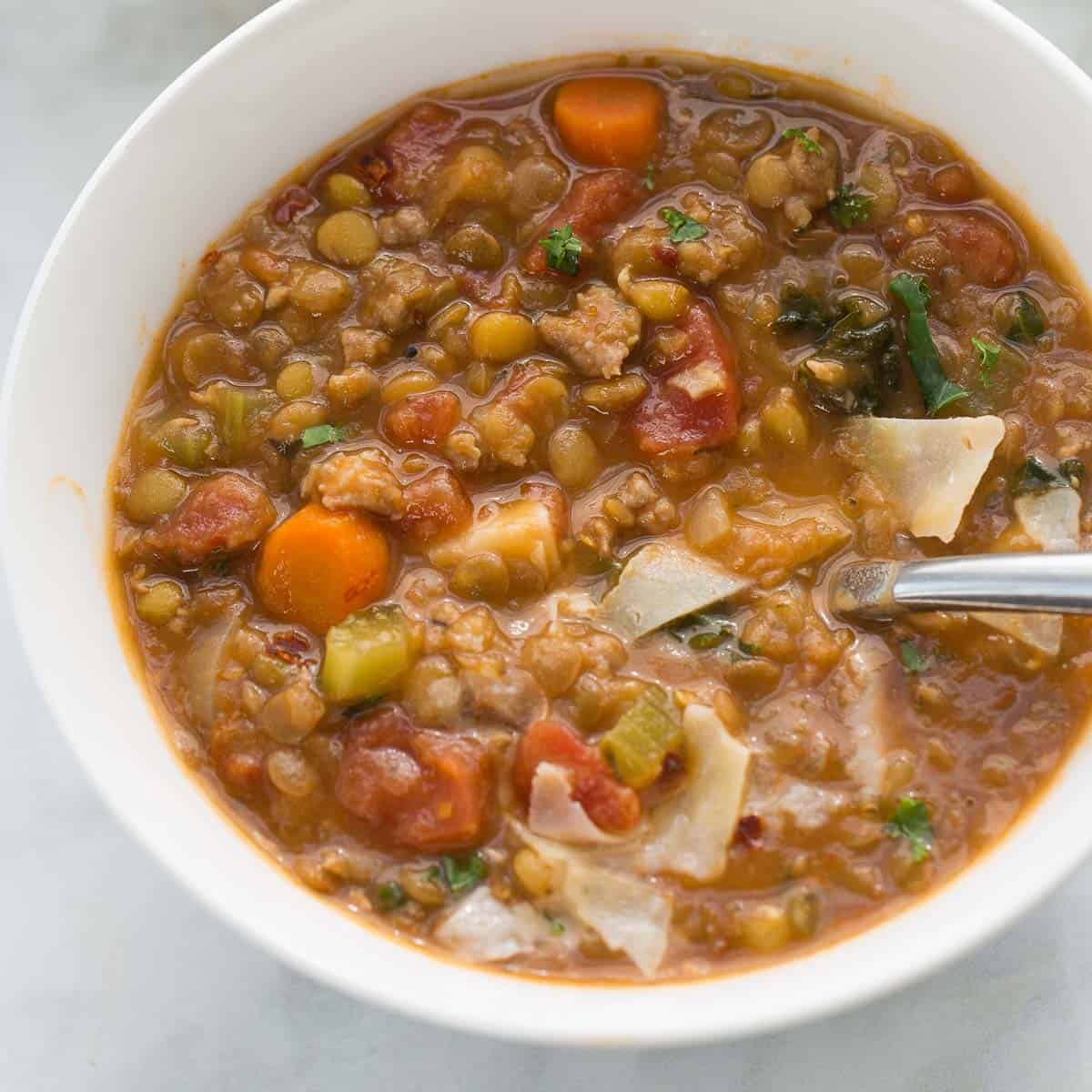 lentil sausage stew in bowl topped with parmesan cheese