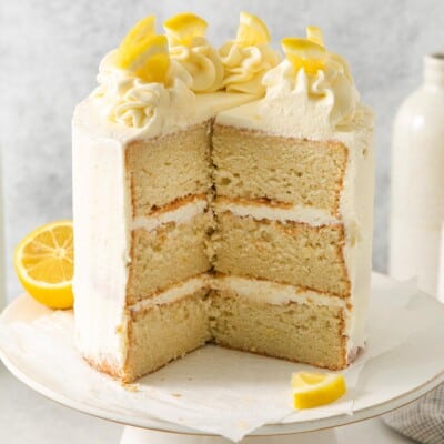 Gluten-free lemon cake on a cake stand, with a large slice out of it and with lemons on top and on the side