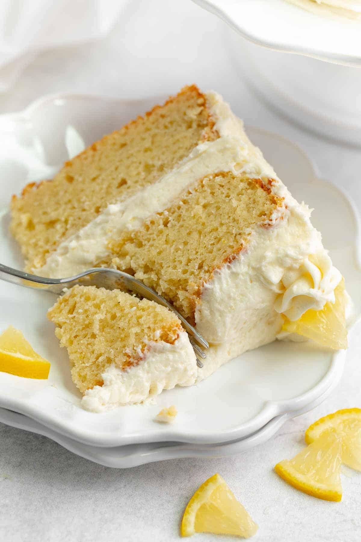 A piece of lemon cake on a plate with a fork cutting into it.