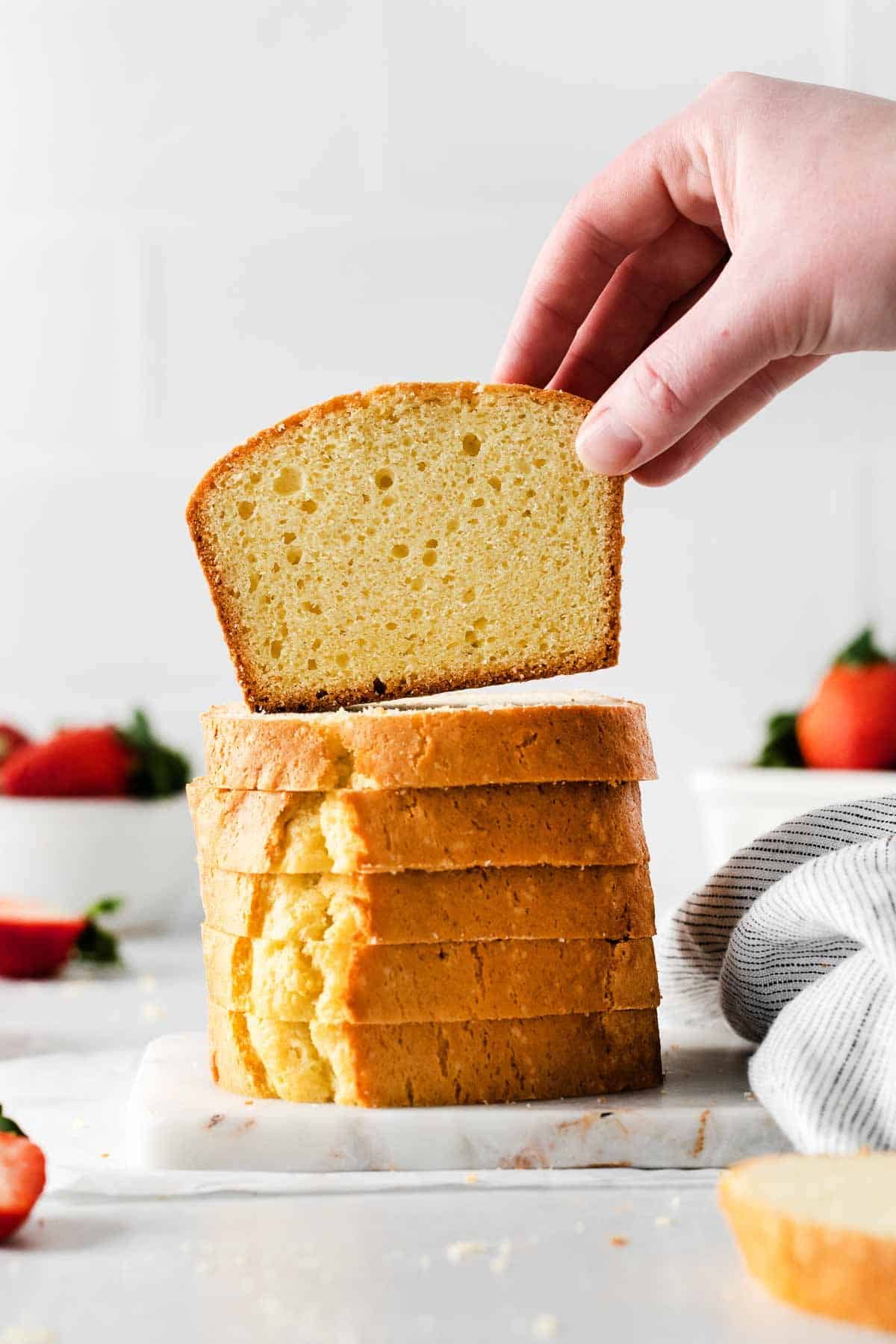 Pound cake slices stacked vertically on a table, with a hand picking up a piece