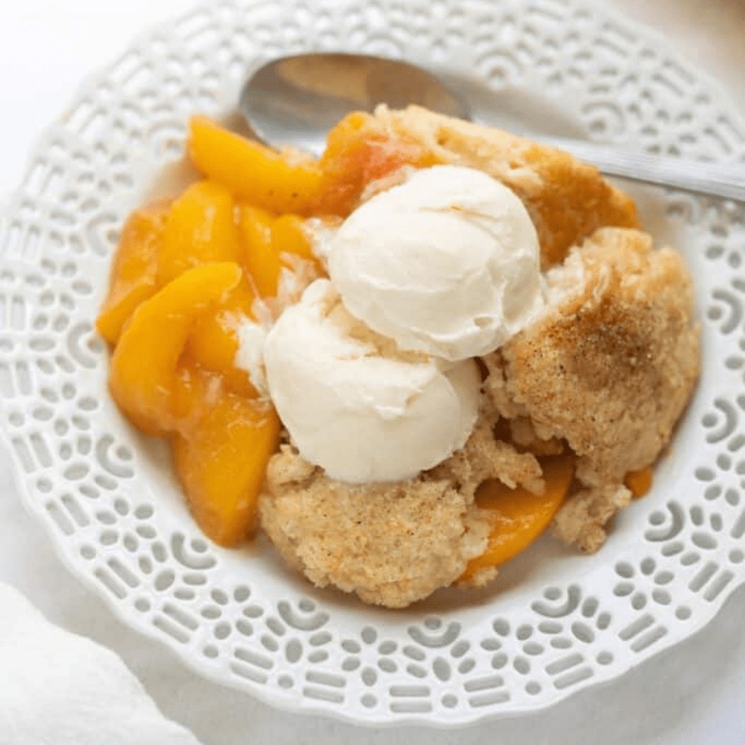 A serving of peach cobbler on a plate, with ice cream on top