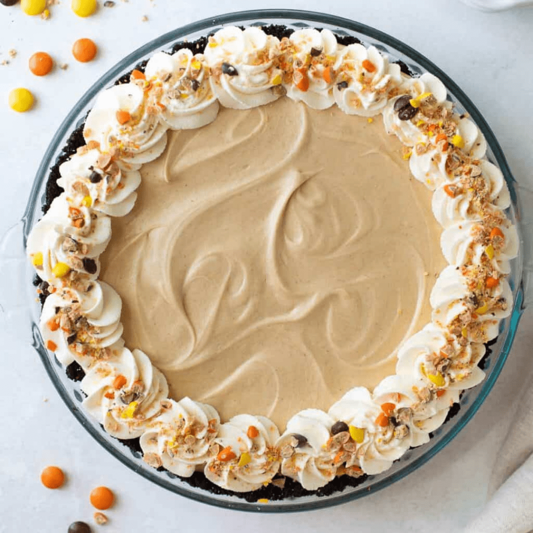 Peanut butter pie in a pie dish, topped with whipped cream and Reese's Pieces