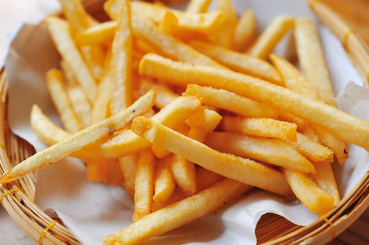 close up basket of french fries on white parchment paper