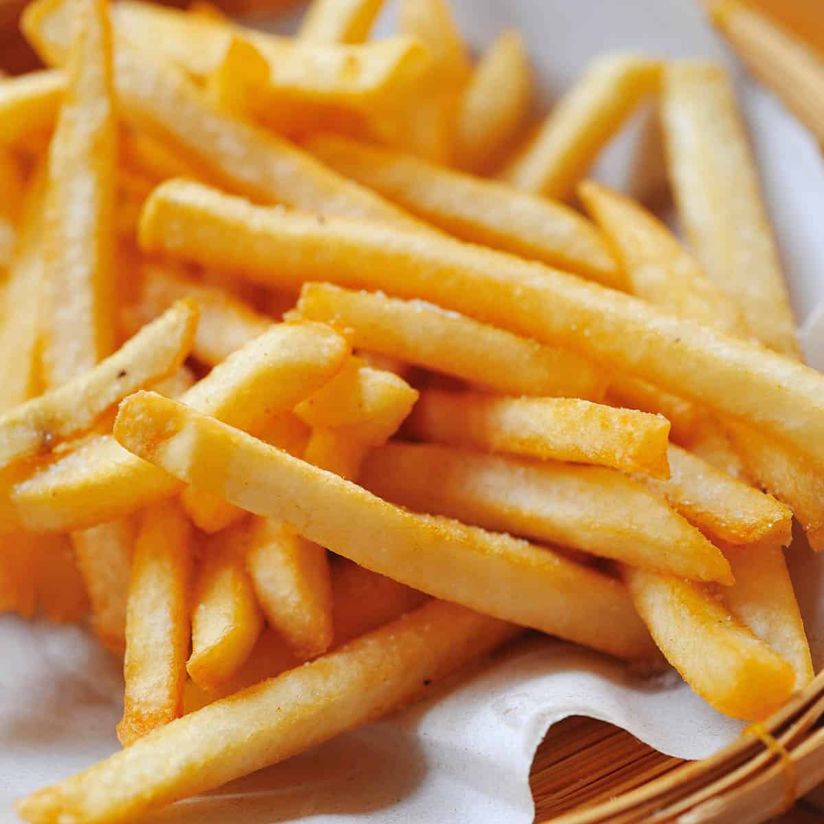 close up basket of french fries on white parchment paper