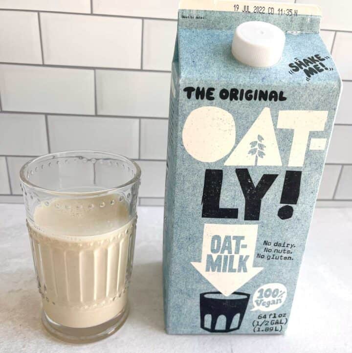 glass of oat milk next to carton of oat milk