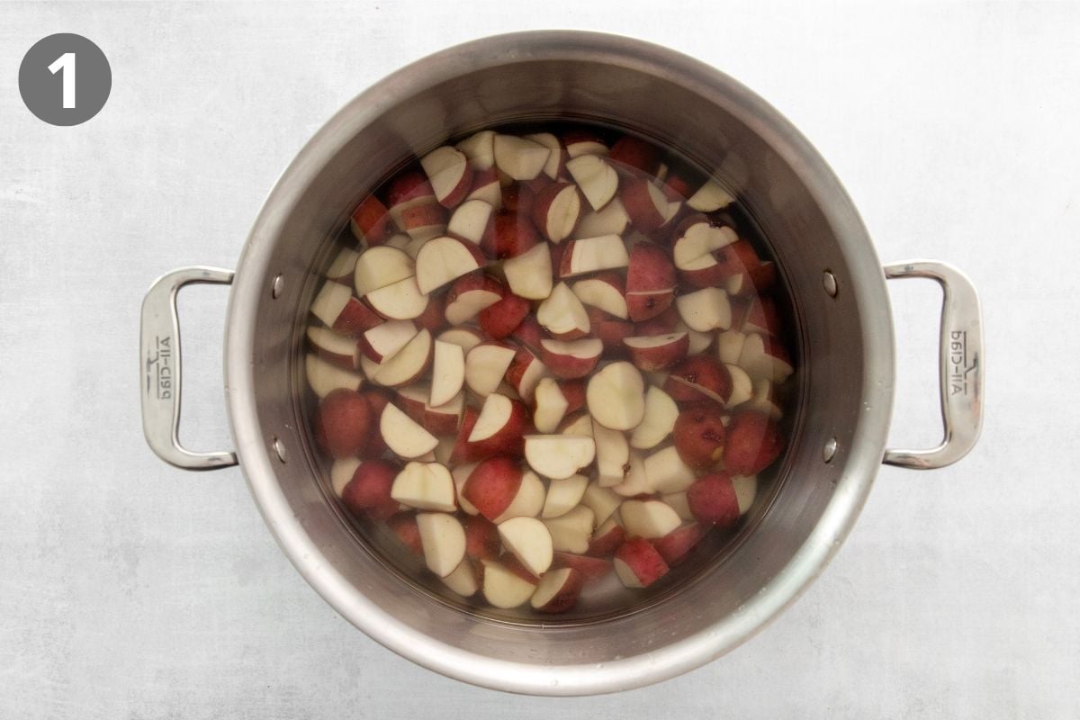 Top-down view of a large pot filled with water and chopped red potatoes. A grey circle with the number 1 is in the upper left corner of the image.