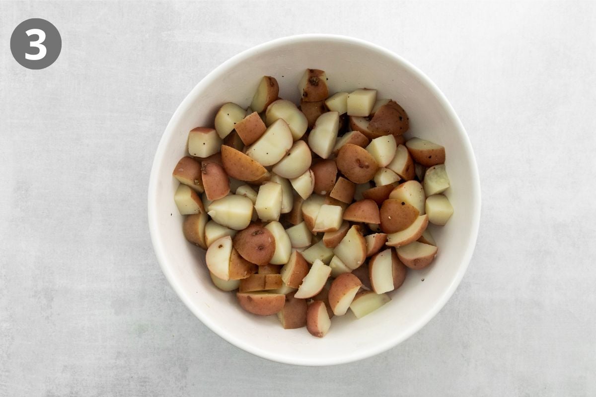 A white bowl filled with chopped, cooked red potatoes sits on a light gray surface. The number 3 appears in a dark circle in the top left corner of the image.