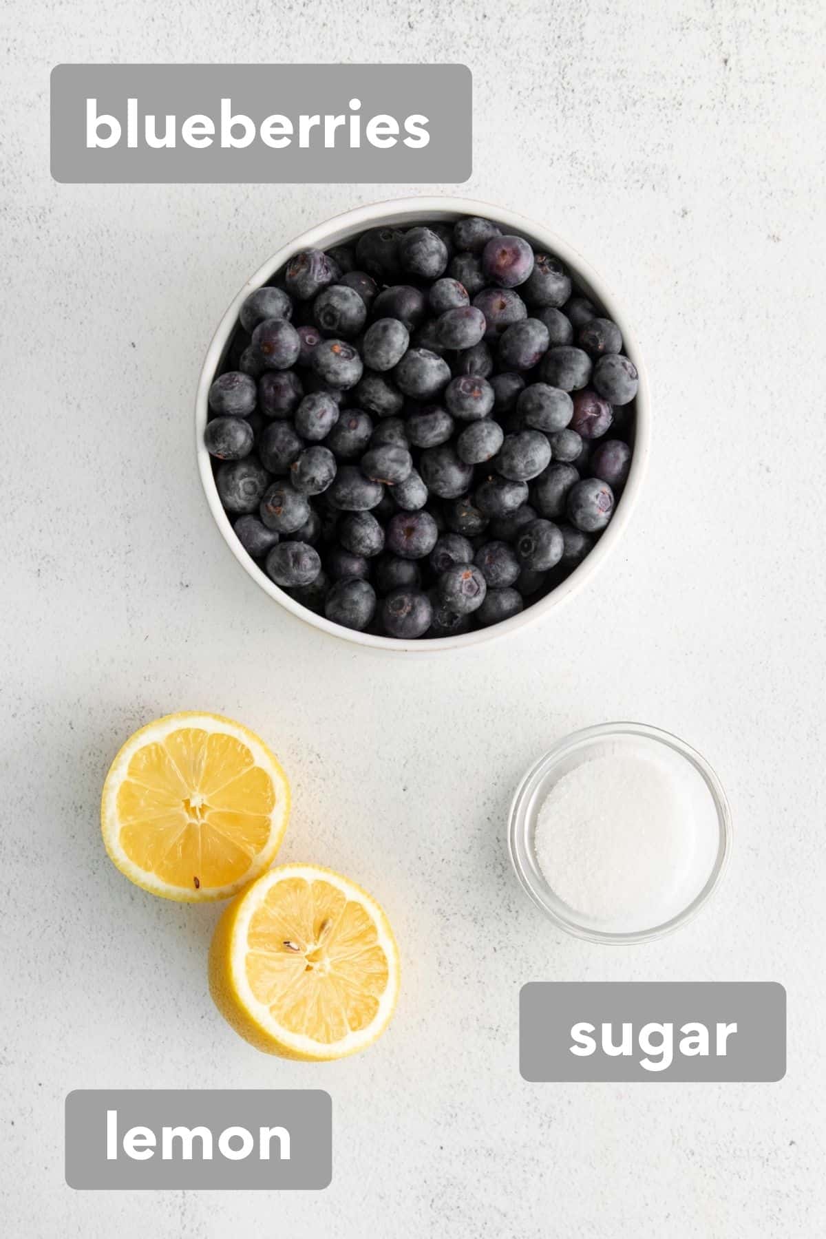 Blueberry compote ingredients, including fresh blueberries, a lemon cut in half, and white sugar