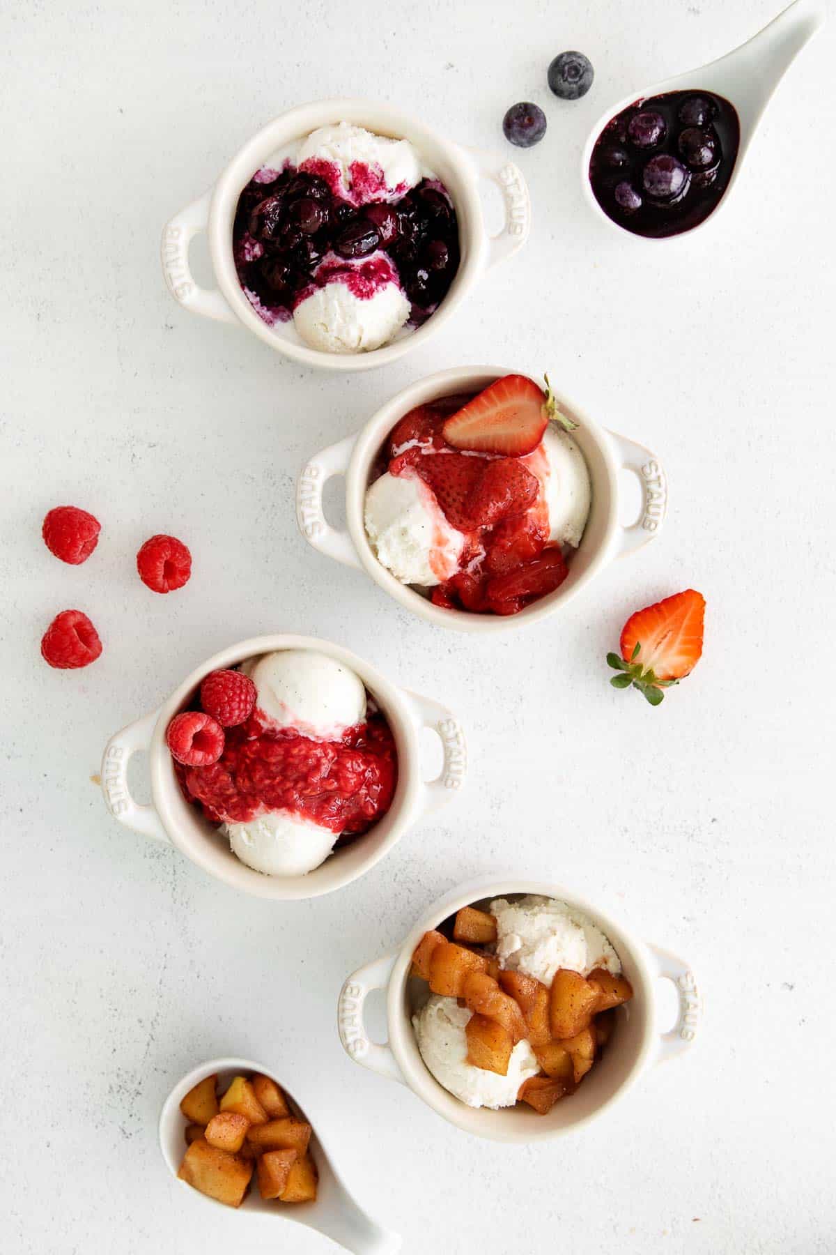 Four ramekins filled with vanilla ice cream and topped with different types of fruit compote