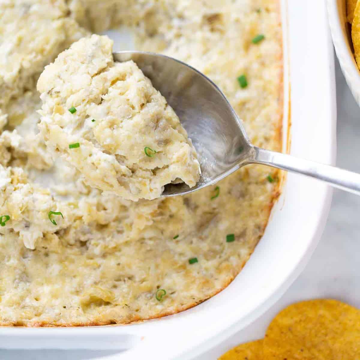 close up image of artichoke dip being scooped with spoon