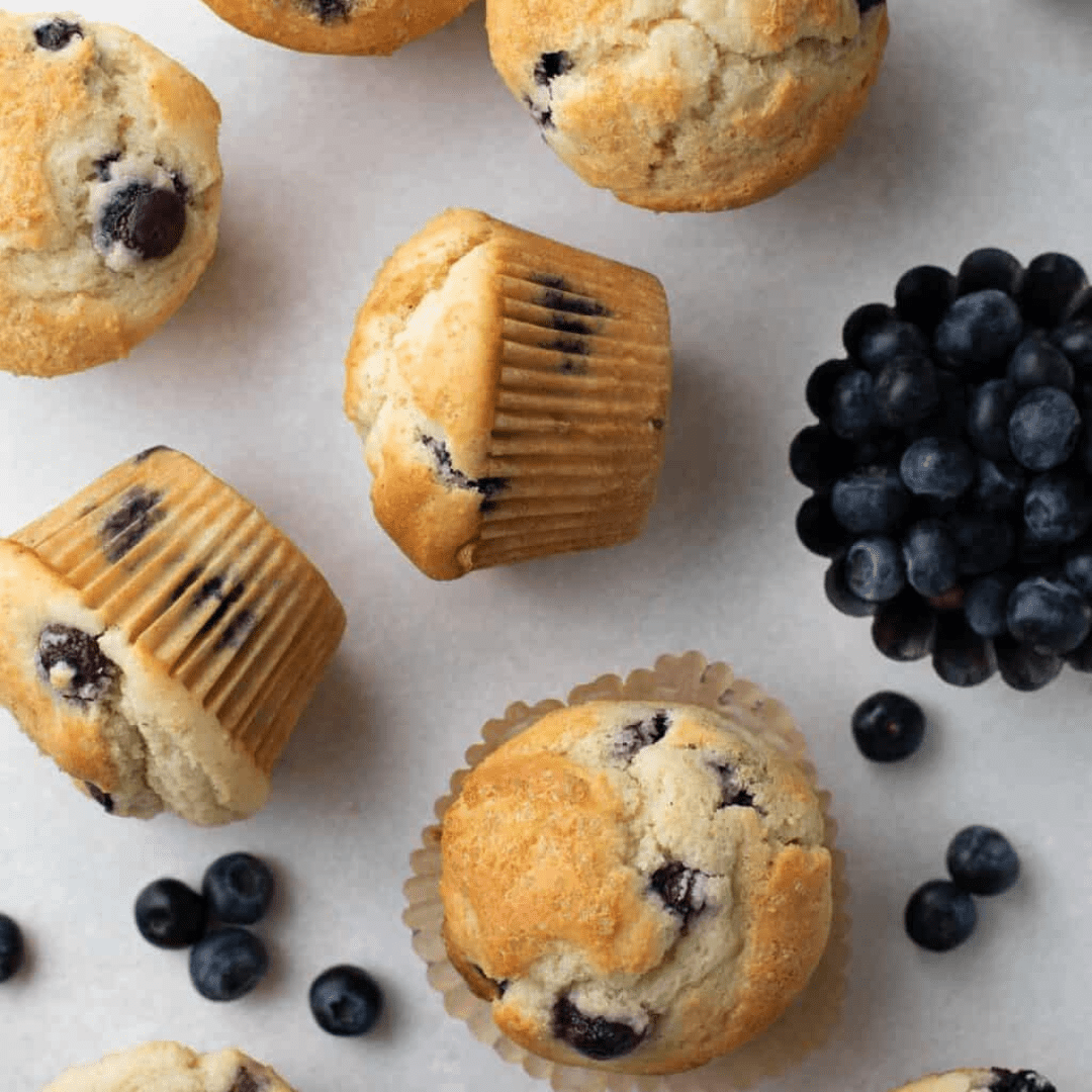 Blueberry muffins on a countertop with blueberries scattered around