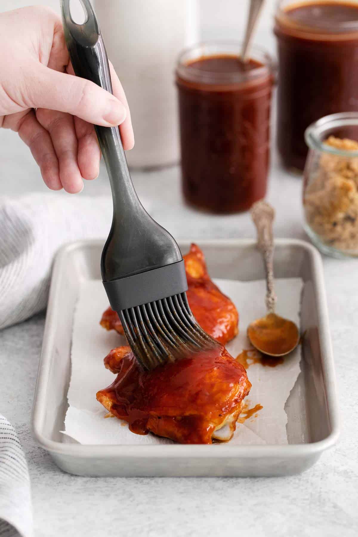 A hand basting a piece of chicken with gluten-free BBQ sauce